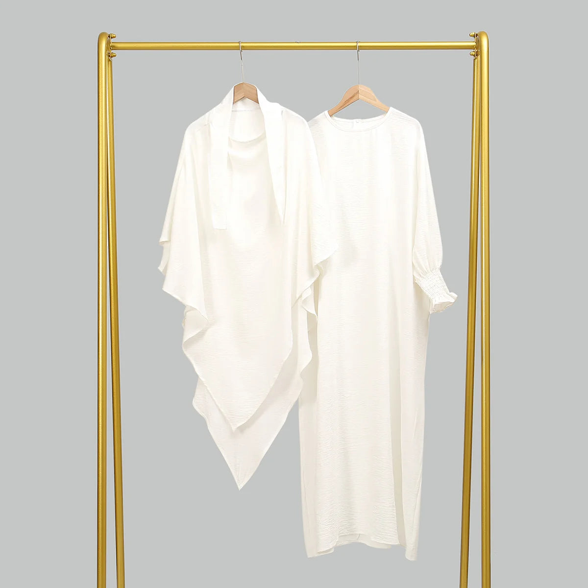 Weiße, elegante Abaya und Khimar-Set auf goldenem Bügel vor grauem Hintergrund.