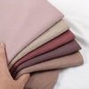 Ein Stapel von vier zerknitterten Schals oder Hijabs in verschiedenen Nuancen von staubigem Rosa und Mauve.