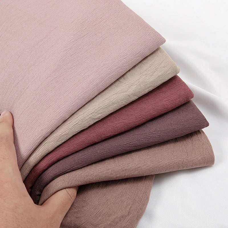 Ein Stapel von vier zerknitterten Schals oder Hijabs in verschiedenen Nuancen von staubigem Pink und Mauve.