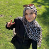 Eine junge Frau mit Leopardenmuster- und Polka-Dot-Baumwollschal und dunkler Kleidung im Freien.