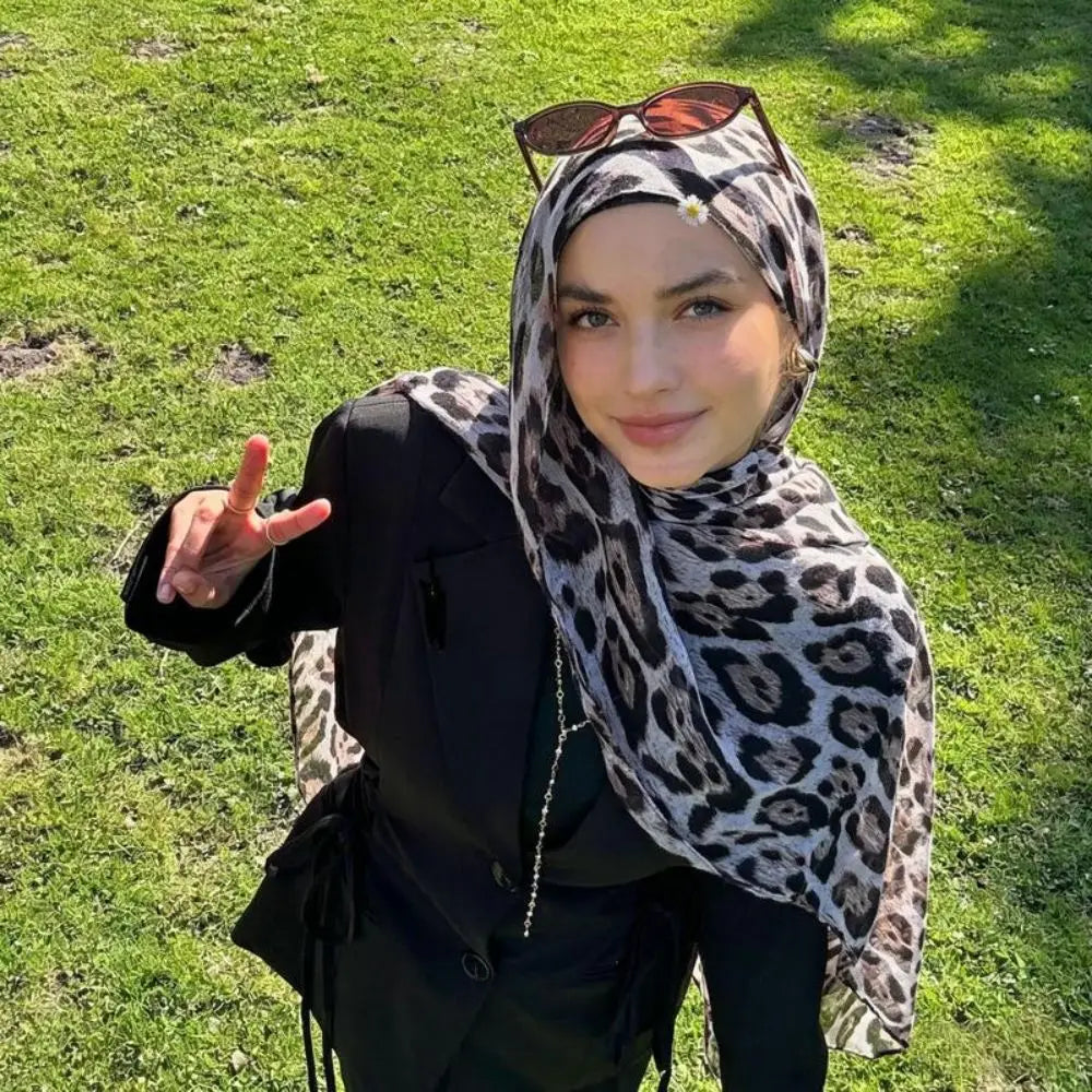 Eine junge Frau mit Leopardenmuster- und Polka-Dot-Baumwollschal und dunkler Kleidung im Freien.