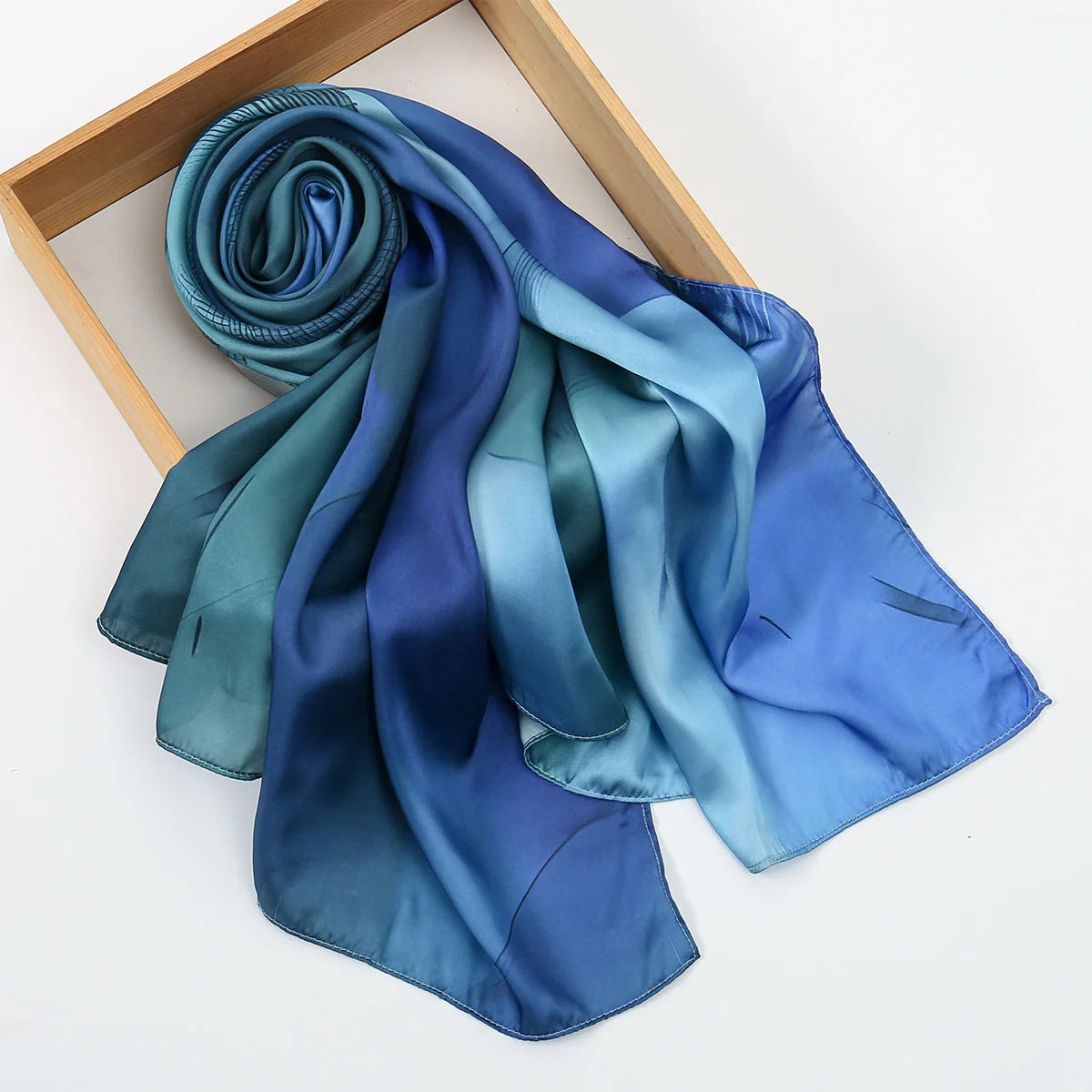 Foulard hijab en soie satinée drapé dans des tons de bleu et sarcelle, exposé sur un cadre en bois.
