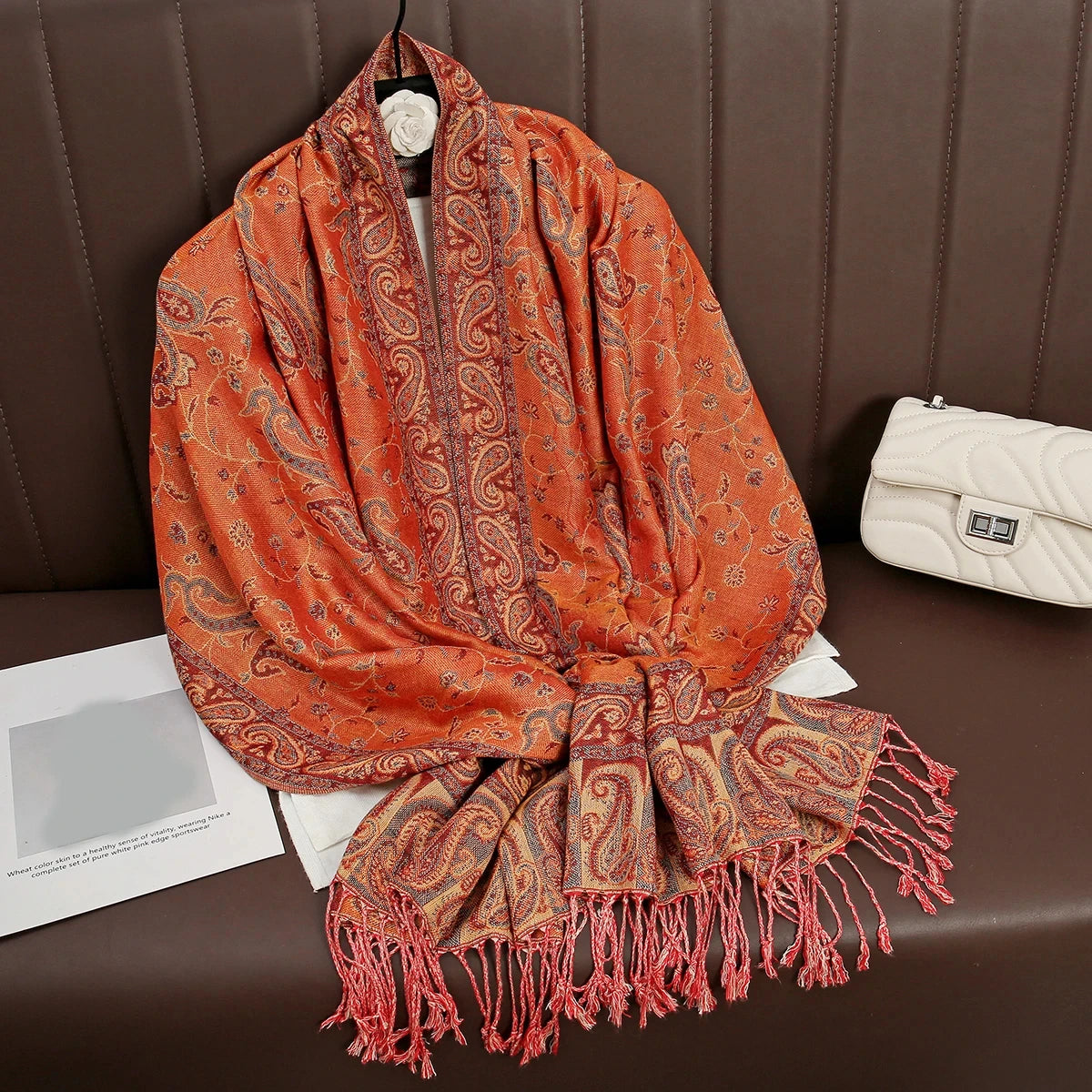 Pañuelo de pashmina naranja y óxido drapeado sobre una superficie de cuero marrón.