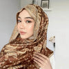 Eine Frau trägt einen eleganten braunen Paisley-Viskose-Hijabschal mit goldenen Verzierungen.