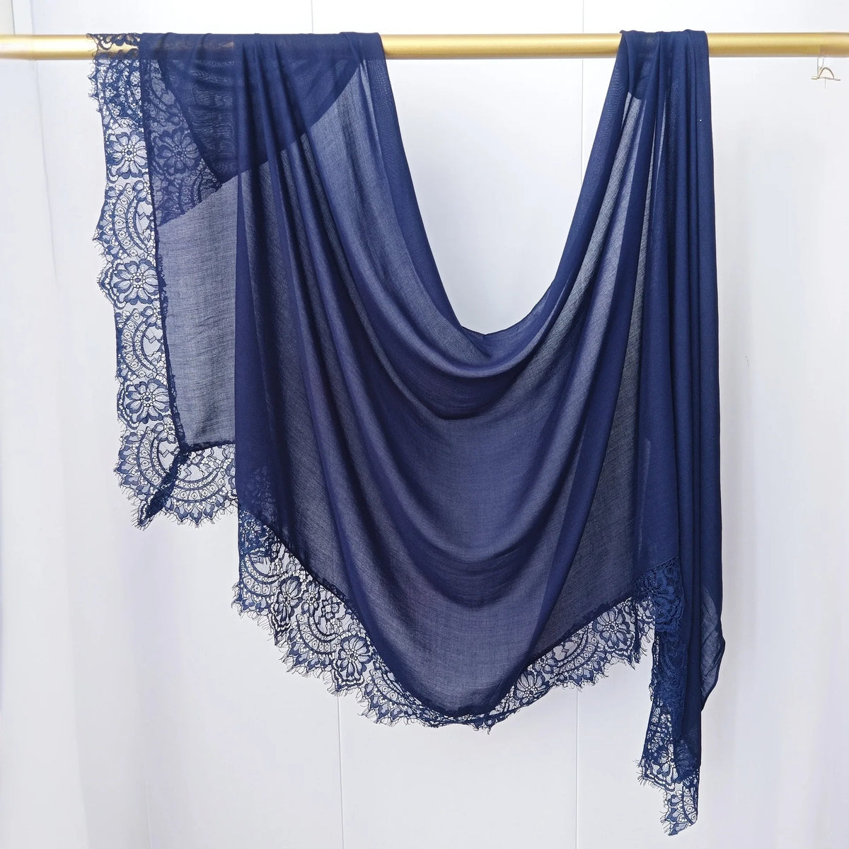 Hijab de encaje azul oscuro drapeado sobre un perchero de madera.