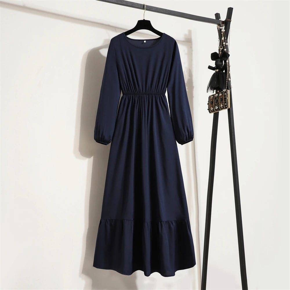 Dunkelblaue Maxi-Kleid mit langen Ärmeln und gerafftem Bund an einem Holzbügel vor einer weißen Wand.