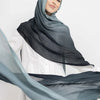 Eine Frau mit grauem Hijab und schwarzem Schal mit durchscheinendem blauem Stoff, der um sie herumfließt.