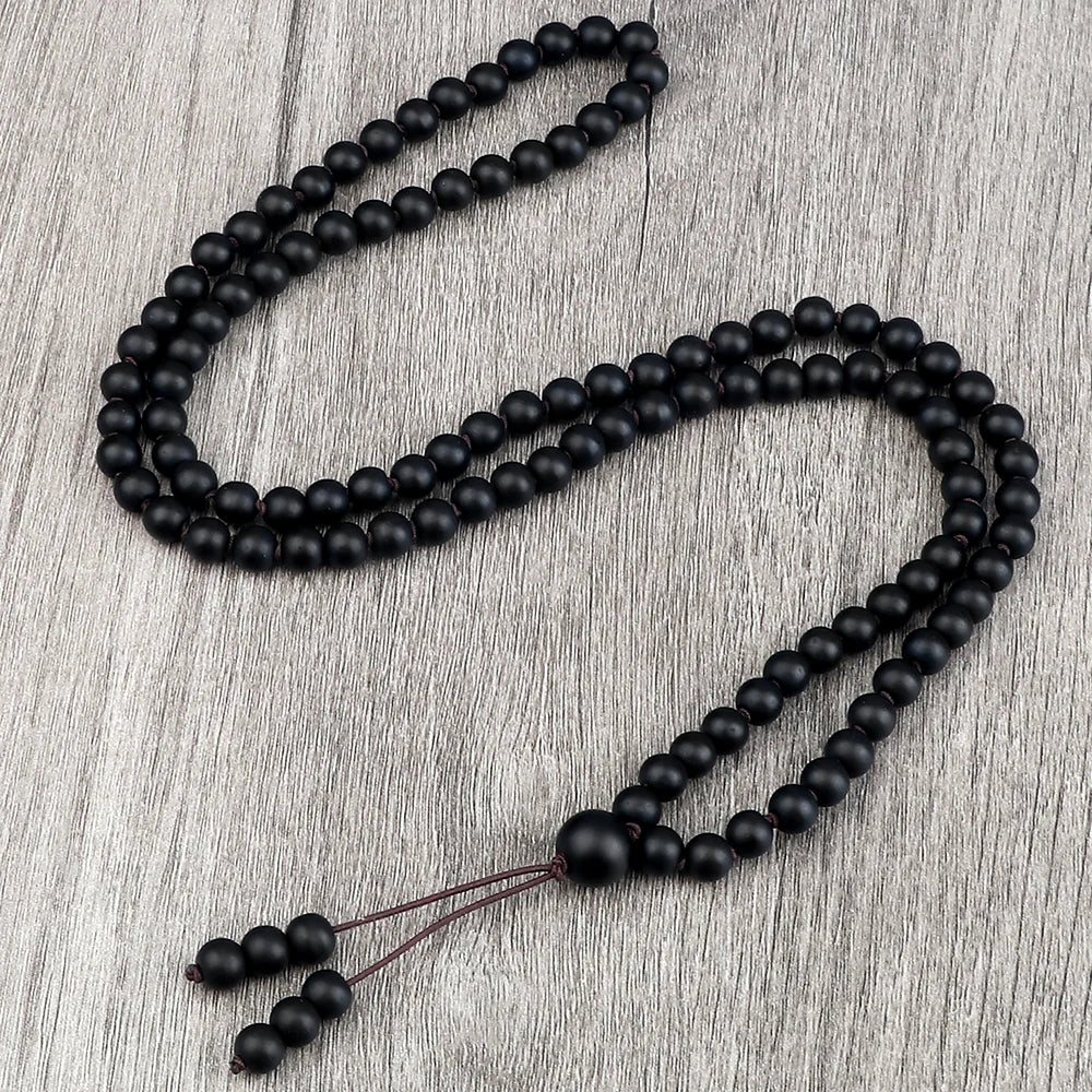 Schwarze Natursteinperlenkette, drapiert auf einer hellen Holzoberfläche.