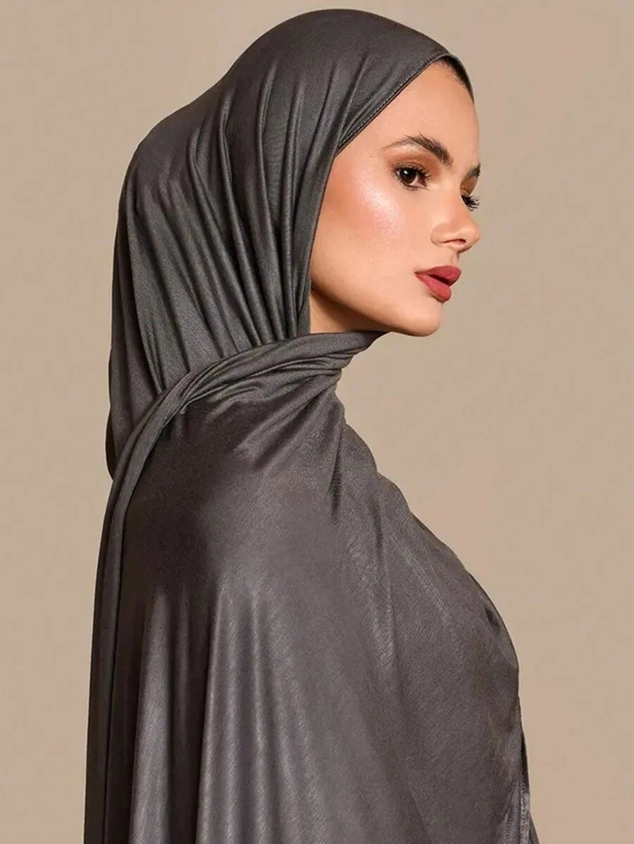 Una mujer vistiendo un pañuelo hijab de jersey modal de color gris carbón drapeado, vista de perfil.