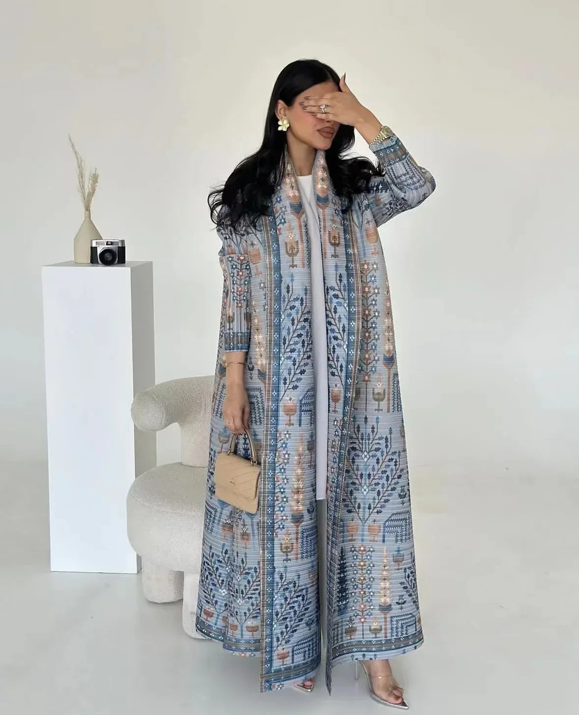 Une femme modélise un long trench-coat plissé bleu et beige à manches longues et col.