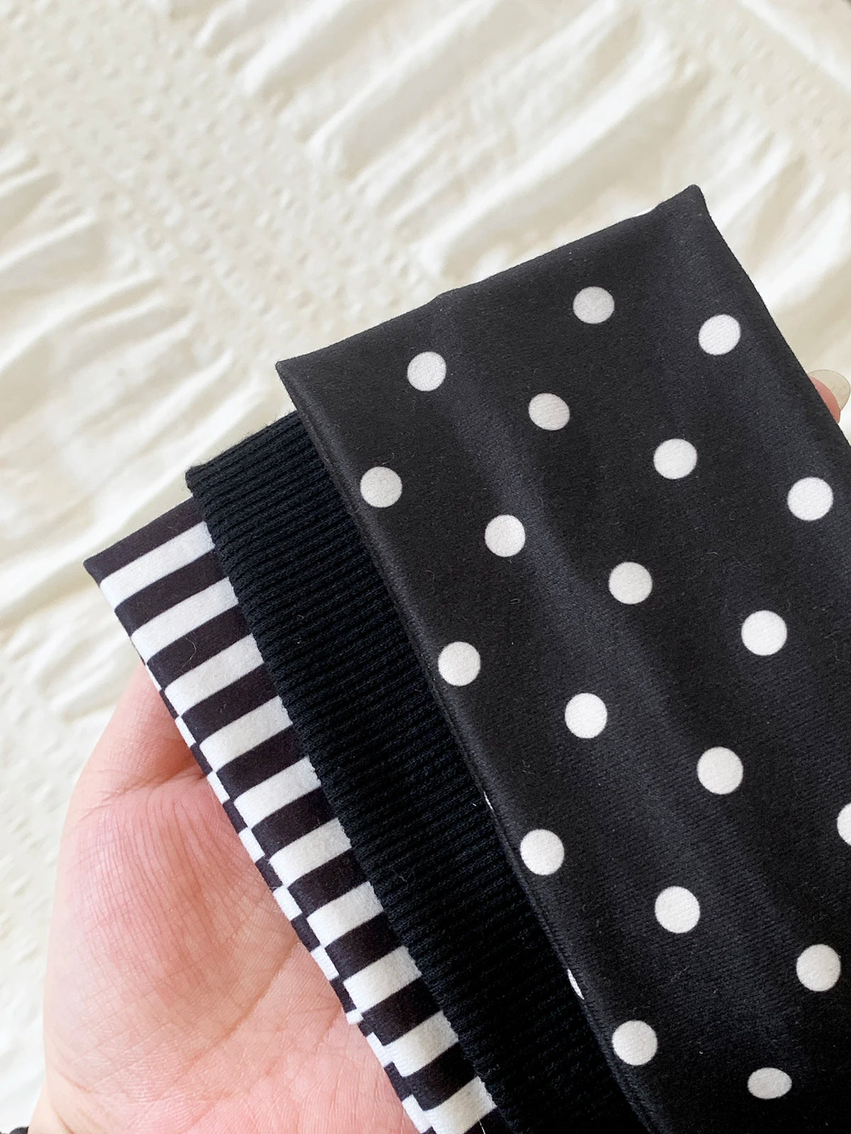Schwarze Polka-Dot-Haube mit gestreiftem Elastikband in der Hand vor weißem Hintergrund