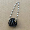 Bolso de mano negro texturizado con detalles dorados y una cadena de pequeñas perlas blancas.