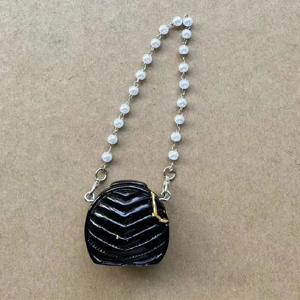Bolso de mano negro texturizado con detalles dorados y una cadena de pequeñas perlas blancas.
