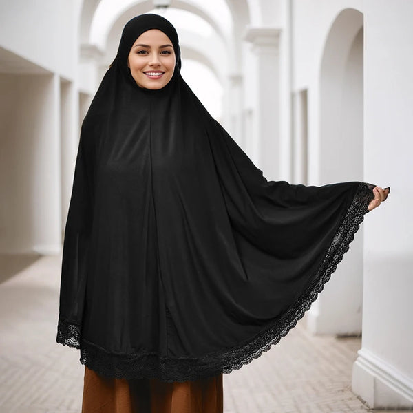 A woman wearing a black full cover instant hijab with lace edges standing in a bright hallway.