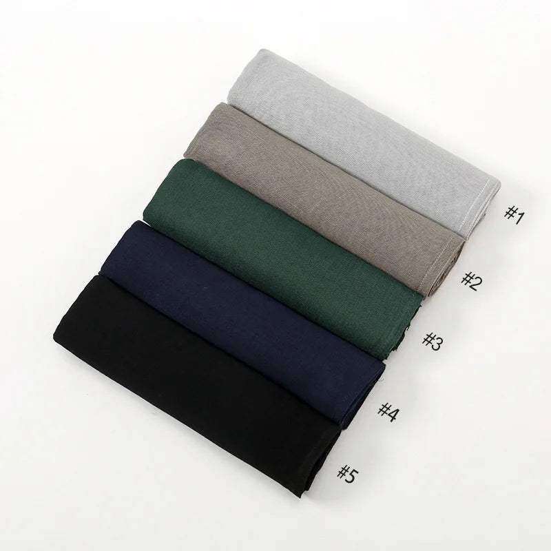 Una pila de cinco pañuelos de hijab de modal rayón de colores sólidos en tonos de gris, verde, azul y negro.