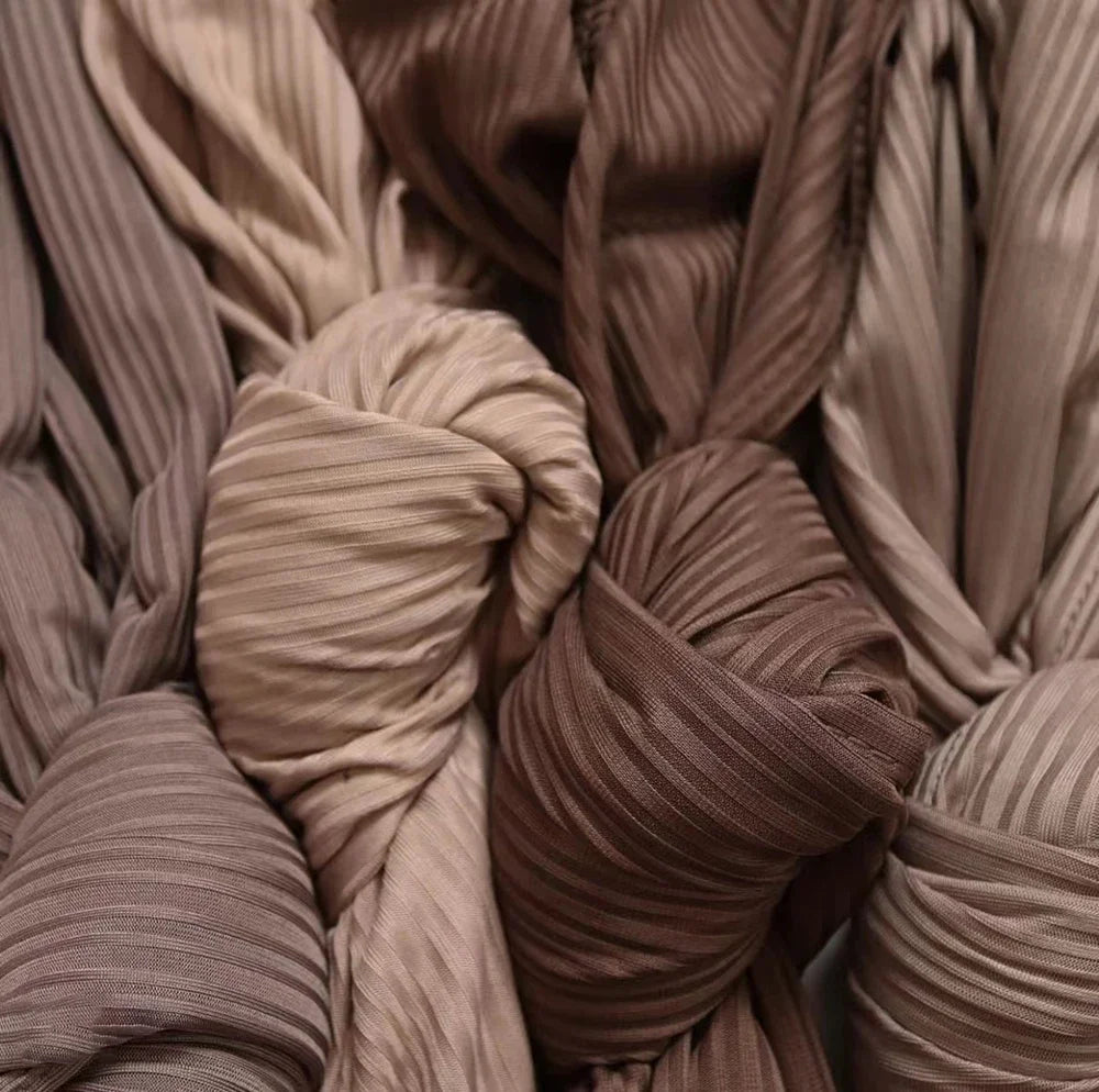 A close-up of multiple rolled ribbed jersey hijab scarves in various shades of beige and brown.