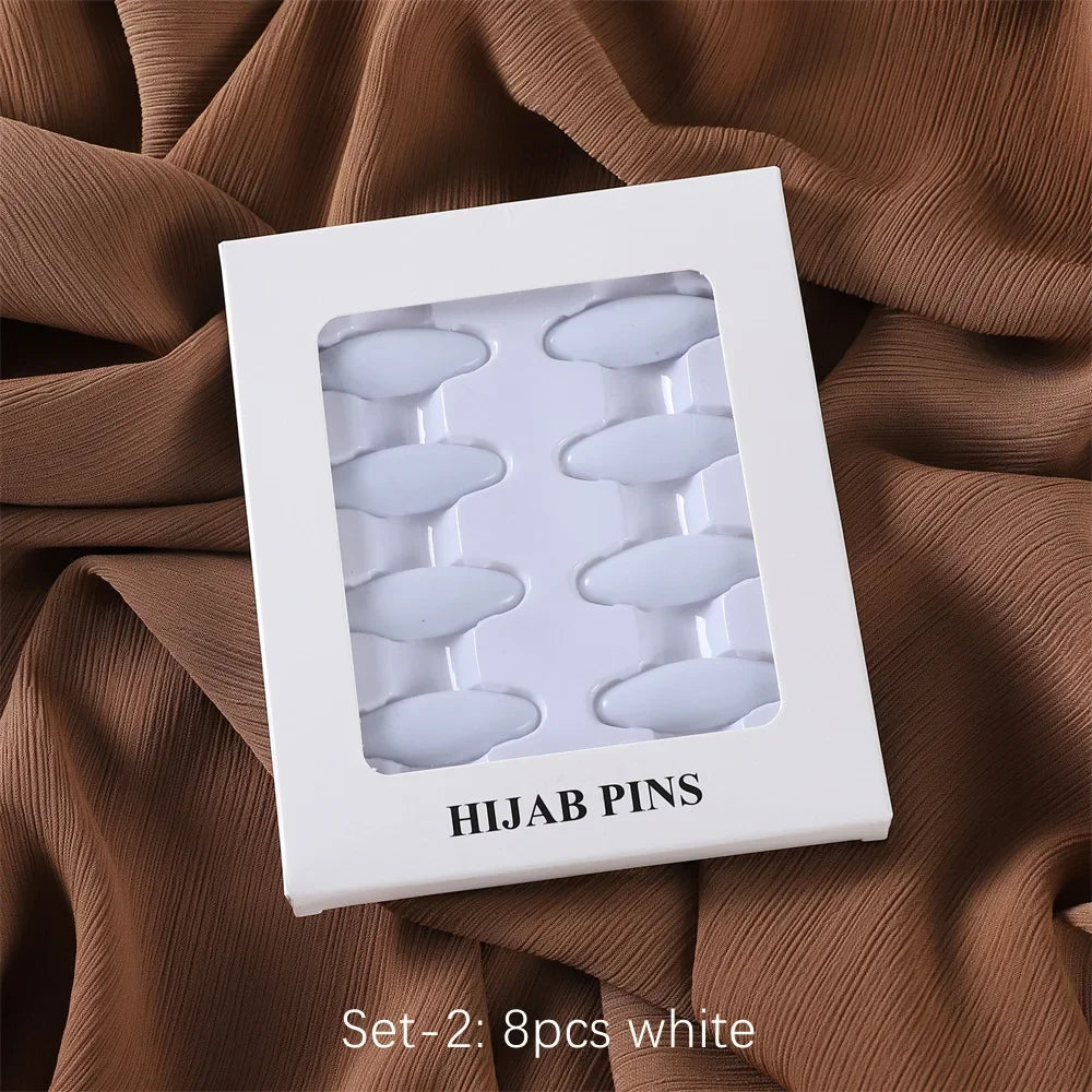 Set of 8 white hijab pins packaged in a white square box on a brown fabric background