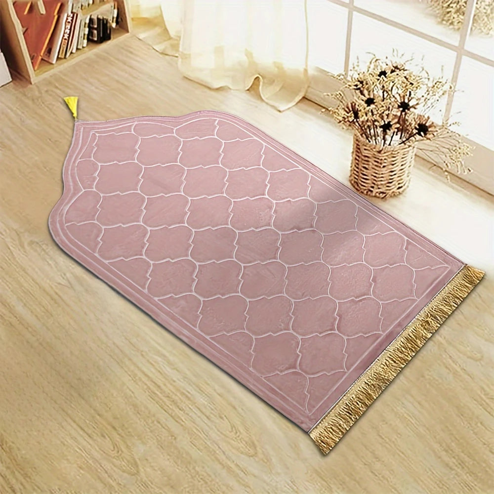 Un tapis de prière rose embossé avec une pompon doré posé sur un plancher en bois clair près d'une fenêtre.
