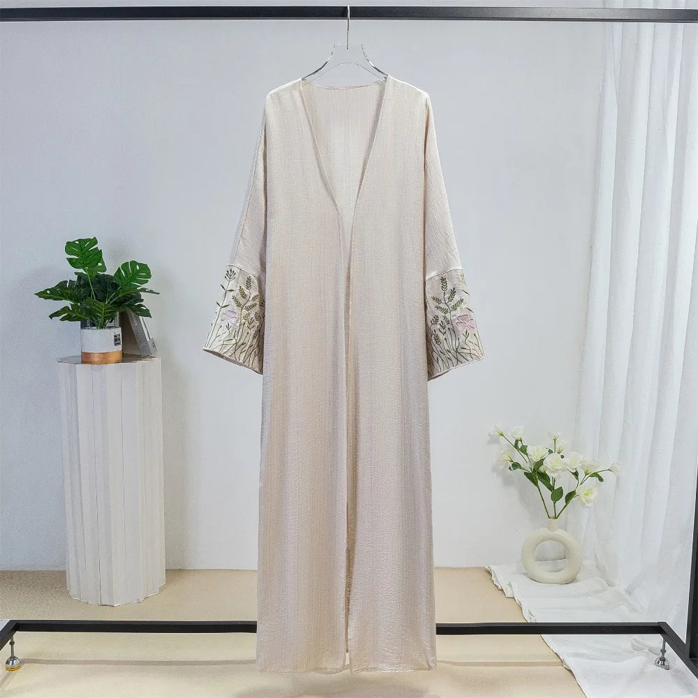 Beige bestickte, weite Kaftan-Abaya an einem Haken vor weißem Hintergrund.