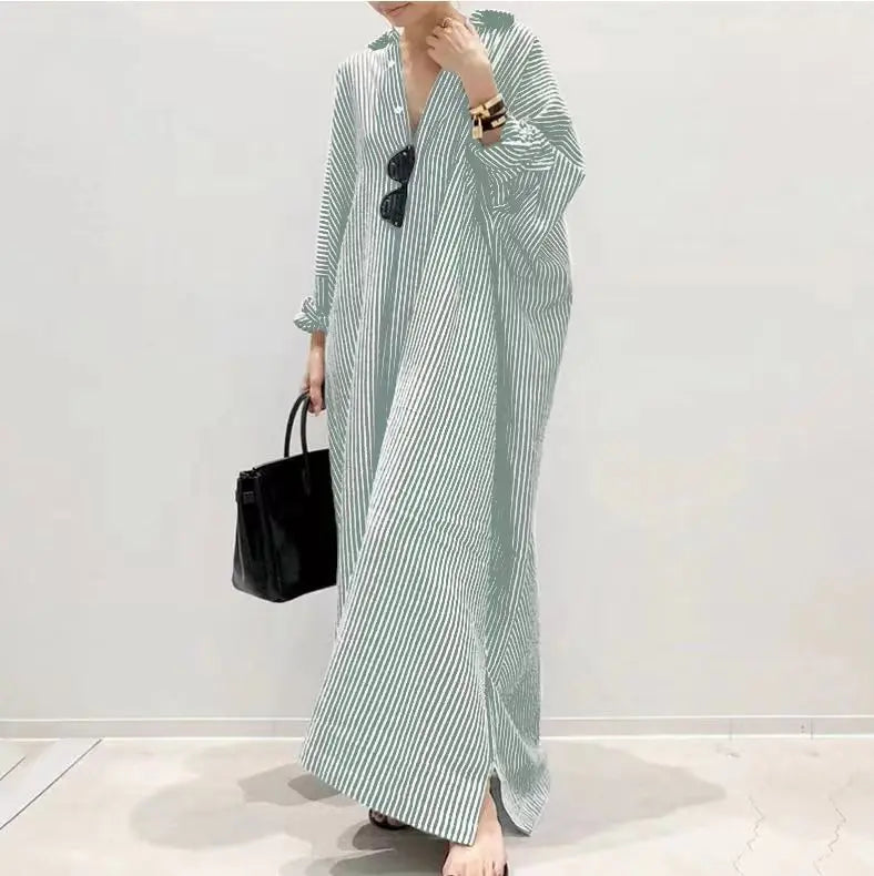 Eine Frau trägt ein langes, fließendes, gestreiftes Baumwollmaxi-Kleid in hellgrünen und weißen Streifen.