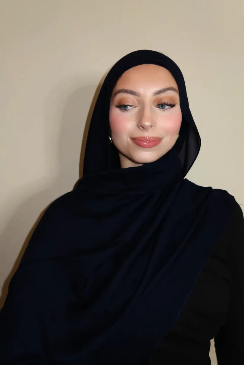 Eine Frau trägt einen schwarzen Gradienten-Rayon-Modal-Hijab-Schal und blickt direkt in die Kamera.