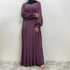 Eine Frau trägt ein elegantes langes lila islamisches Kleid und einen grünen Hijab.