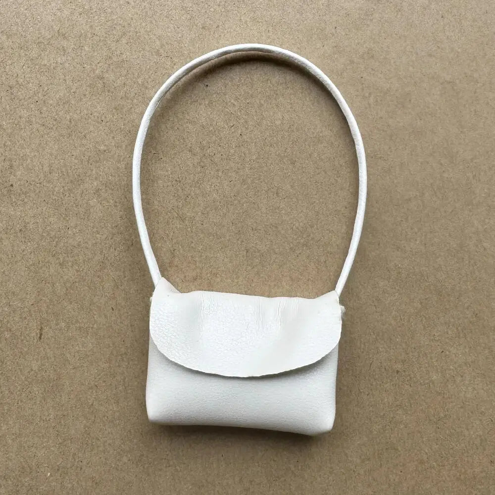 Un accesorio de bolso de cuero blanco con una correa delgada, mostrado contra un fondo marrón.