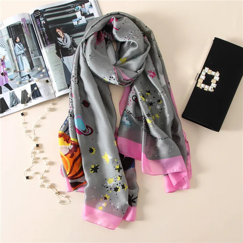 Fließender Seidenschal (Pareo) in Grau und Pink mit Sternmuster, neben einer schwarzen Clutch und einer Zeitschrift.