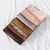 A stack of three elegant watercolor print modal scarves in shades of peach, beige, and brown.