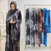 Eine Frau in grauer Abaya und Hijab steht neben einer Ausstellung eleganter Blumen-Abaya- und Hijab-Sets.