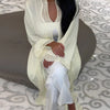 Una mujer vistiendo un elegante kaftan de manga larga, color verde claro con ribetes de encaje blanco y pantalones blancos.