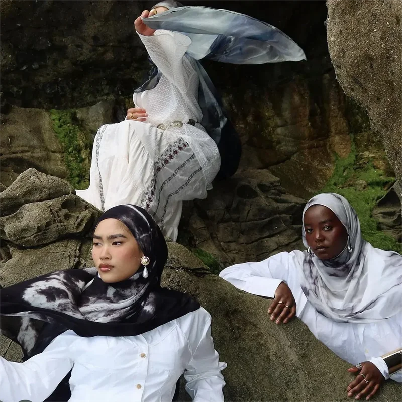 Drei Frauen in weißer Kleidung und Hijabs posieren vor einem felsigen Hintergrund.