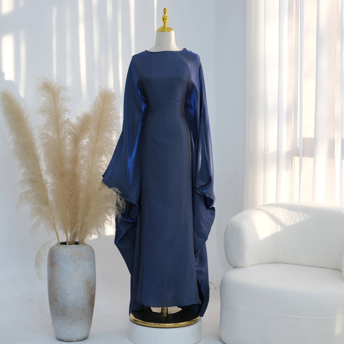 Elegantes dunkelblaues Kaftan-Kleid auf einem Mannequin neben getrocknetem Pampasgras und einem weißen Sessel.