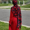 Una mujer vistiendo un largo vestido rojo y un pañuelo hiyab de gasa floral en rojo y negro