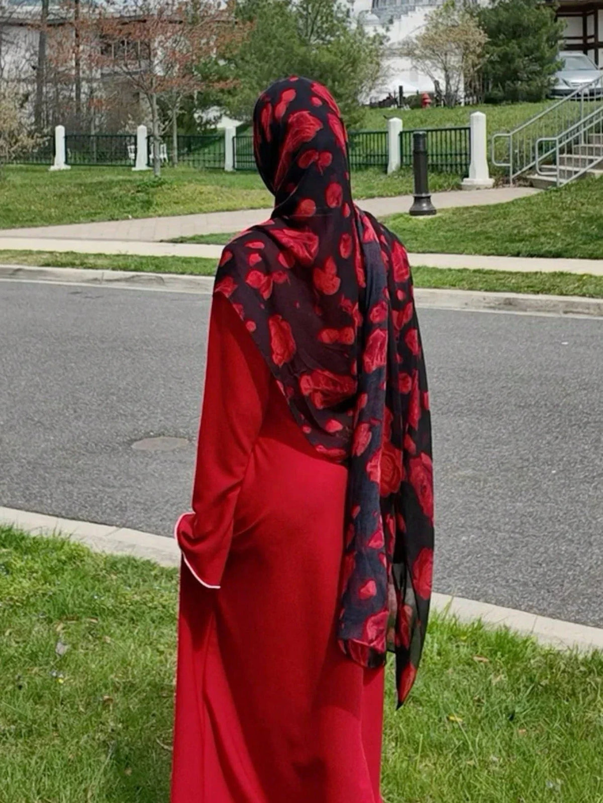 Una mujer vistiendo un largo vestido rojo y un pañuelo hiyab de gasa floral en rojo y negro
