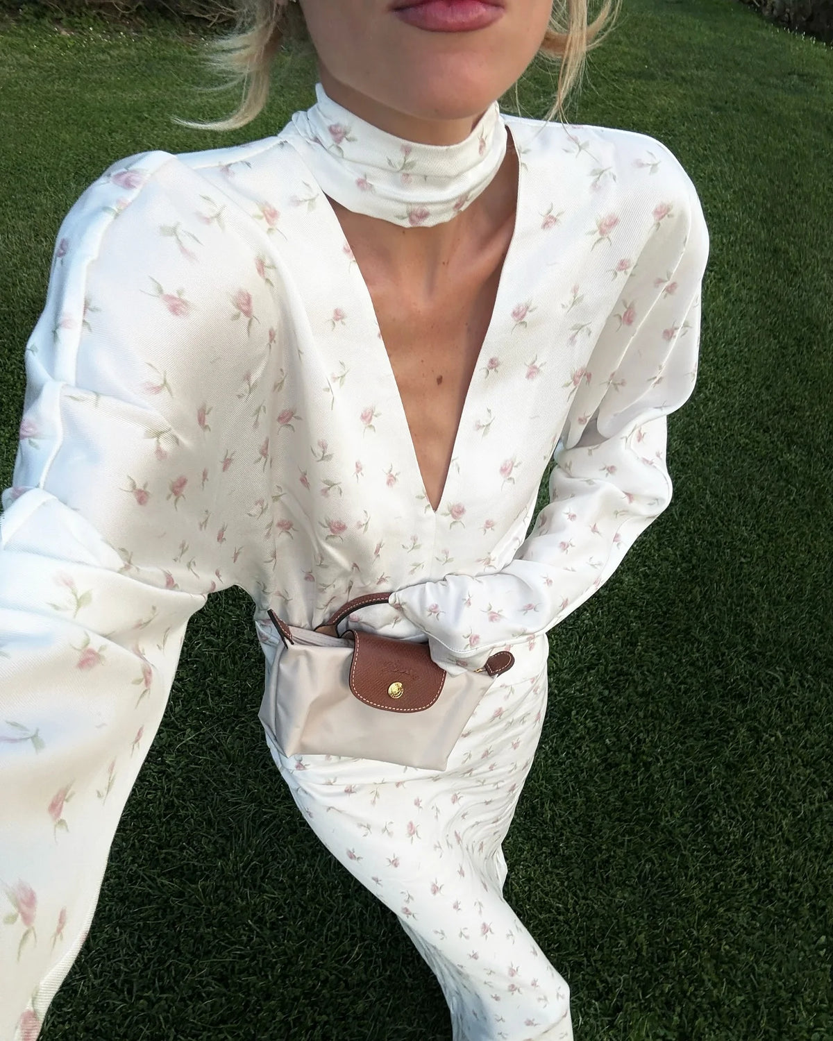Una mujer vistiendo un vestido largo de satén estampado floral blanco con cuello alto y mangas largas, sosteniendo una pequeñ