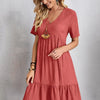 Eine Frau modelliert ein terracottarosa V-Ausschnitt A-Linien-Minikleid mit gerafftem Saum und einem breitkrempigen Hut.