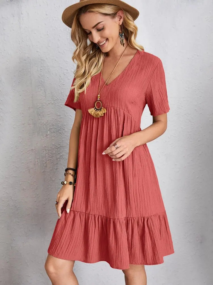 Eine Frau modelliert ein terracottarosa V-Ausschnitt A-Linien-Minikleid mit gerafftem Saum und einem breitkrempigen Hut.