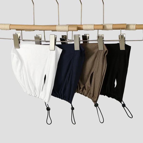 A display of four adjustable modal hijab caps in white, navy blue, olive green, and black hanging from a wooden rack.