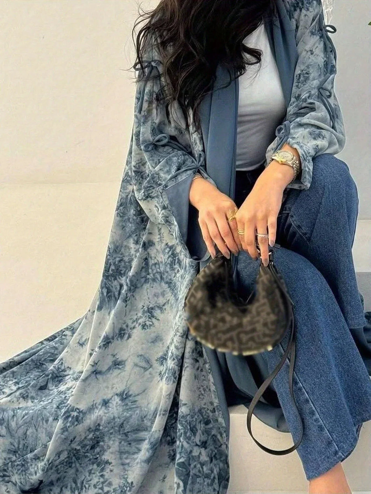 Eine Frau trägt einen blauen Blumen-Tie-Dye-Kaftan über einem weißen Oberteil und Jeans.