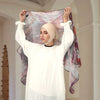 Eine Frau in einem weißen Langarmtop und einem beigen Hijab, die ein durchsichtiges lila Aquarell-Chiffon hält.