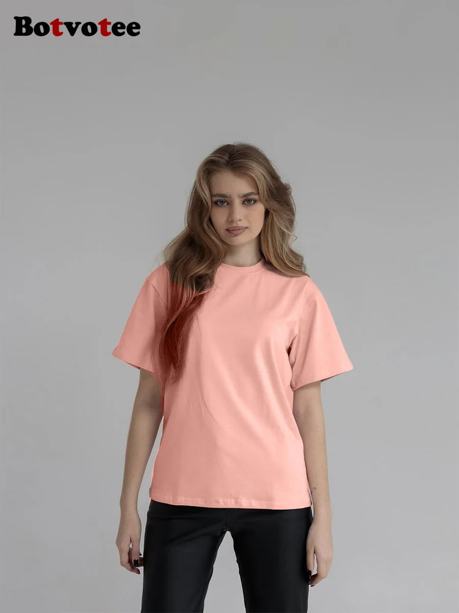 Una modelo vistiendo una camiseta básica de algodón oversize de color melocotón claro y pantalones negros.