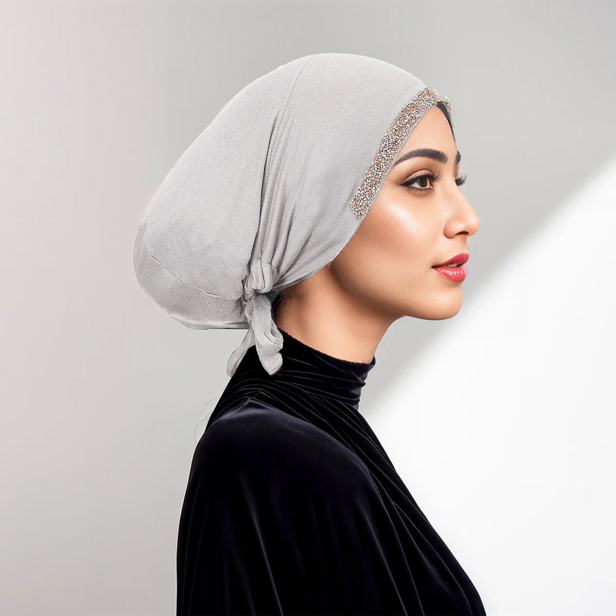 Eine Frau trägt einen hellgrauen, drapierten Hijab mit Strassrand und ein schwarzes Samt-Oberteil.