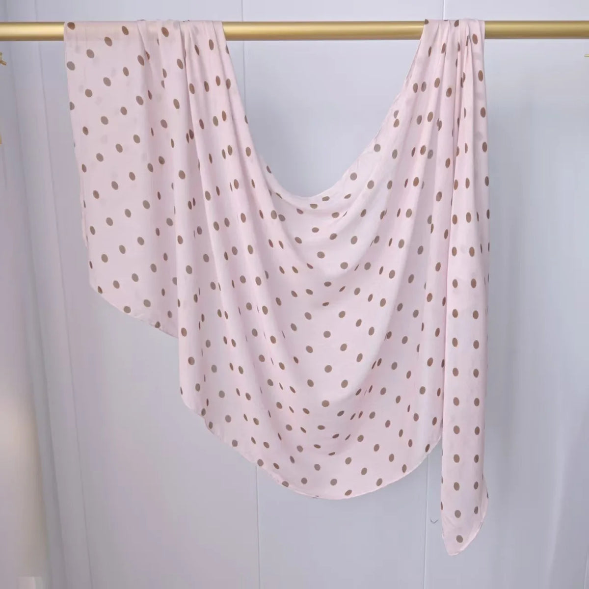 Helles rosa Hijab-Tuch mit kleinen goldenen Polka Dots, über einer Holzleiste