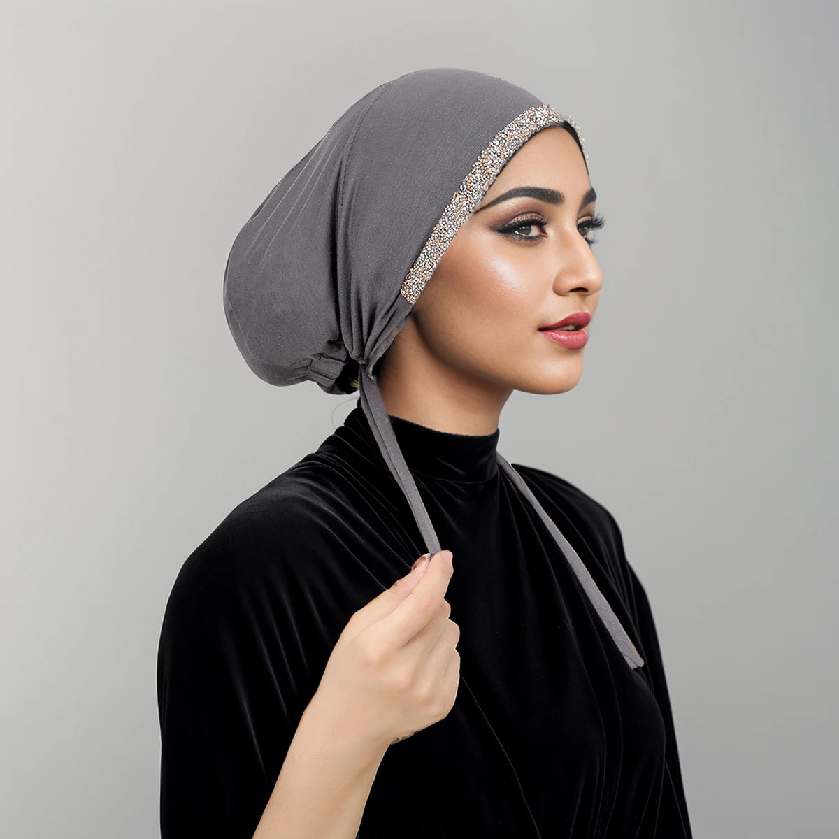 Eine Frau trägt einen grauen Hijab mit Diamantbesatz und ein schwarzes Samt-Oberteil.