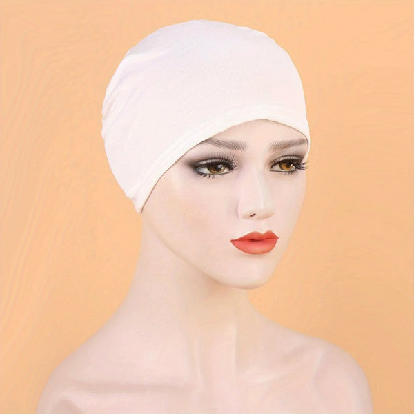 A model wearing a white classic stretch jersey turban cap against a light orange background.