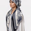 Une femme portant un hijab carré à motif bleu marine et crème drapé sur sa tête et son cou.