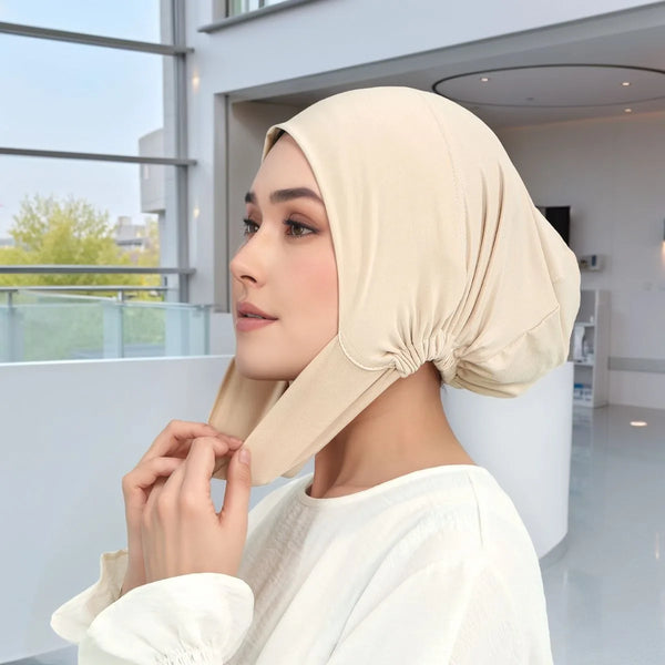 A woman wearing a beige soft cotton milk silk inner hijab cap in a bright indoor setting.