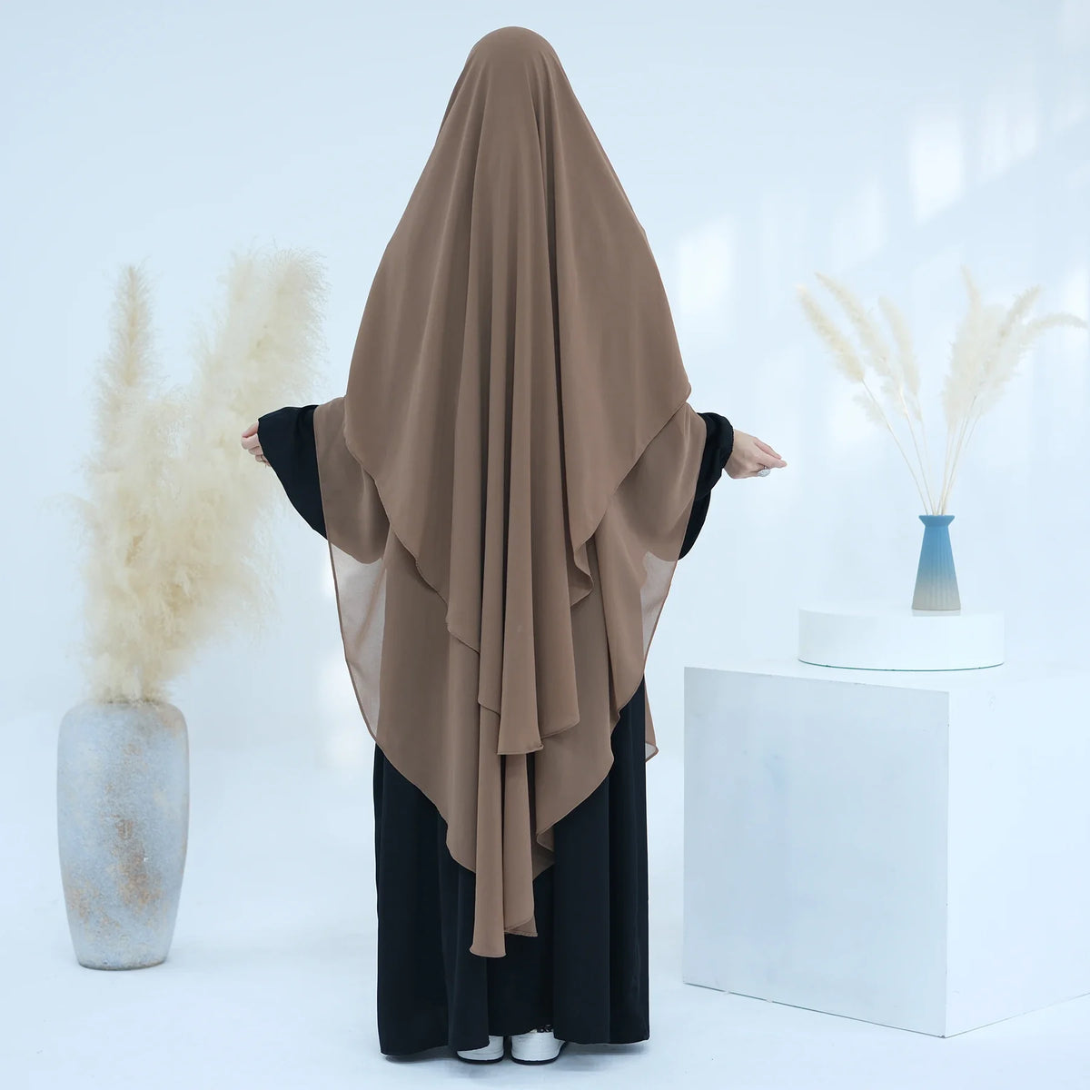 Eine Frau trägt einen braunen, zweilagigen Chiffon-Niqab und schwarze Kleidung in einem hellen Studio.