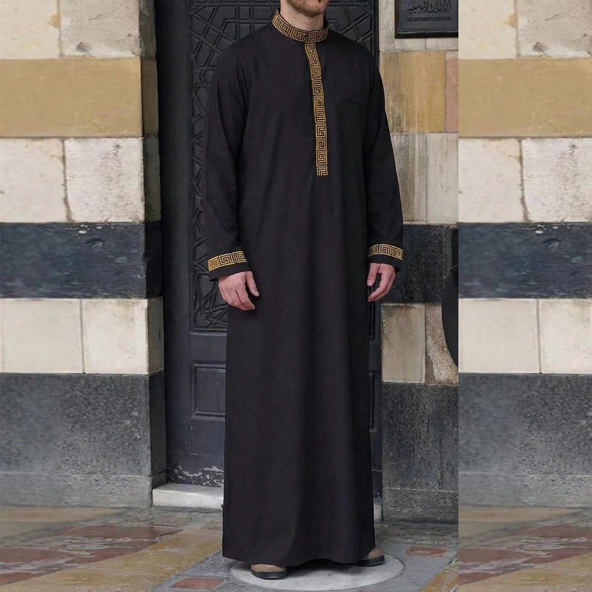 A black Moroccan embroidered men's thobe jellaba worn by a person standing in front of a stone doorway.